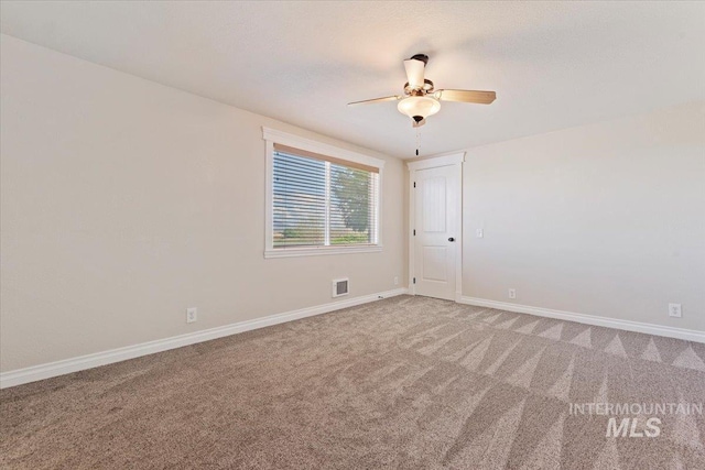 empty room with carpet floors, a ceiling fan, baseboards, and visible vents