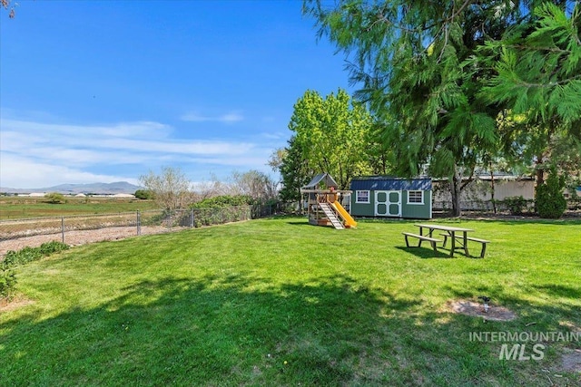 view of yard with fence, a shed, a mountain view, a playground, and an outdoor structure