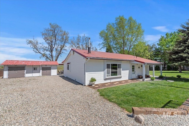 single story home with a detached garage, an outdoor structure, metal roof, and a front yard