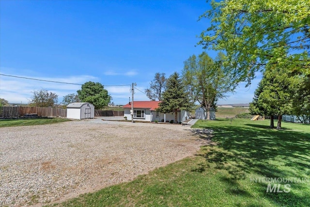 view of yard featuring a storage unit, an outdoor structure, dirt driveway, and fence