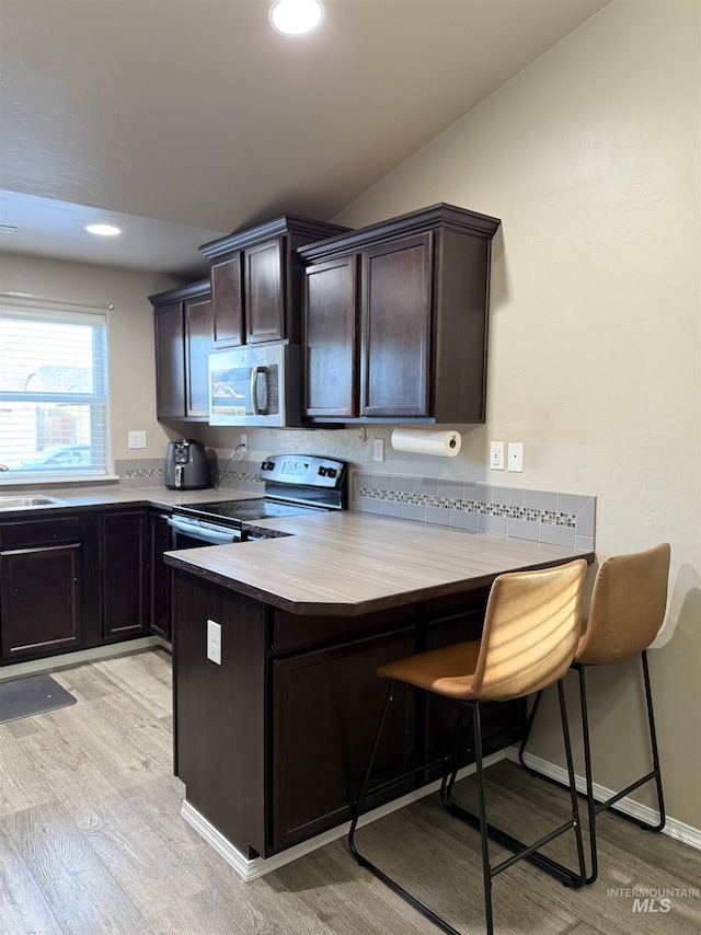 kitchen featuring lofted ceiling, a kitchen bar, stainless steel appliances, light hardwood / wood-style floors, and kitchen peninsula