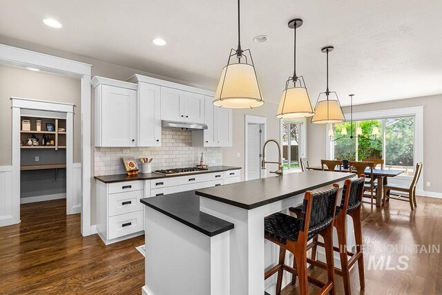 kitchen featuring stainless steel gas cooktop, dark wood finished floors, dark countertops, and tasteful backsplash