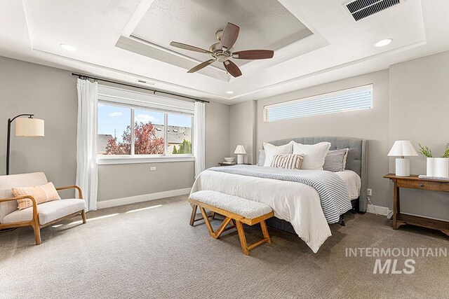 carpeted bedroom featuring a tray ceiling, visible vents, baseboards, and multiple windows