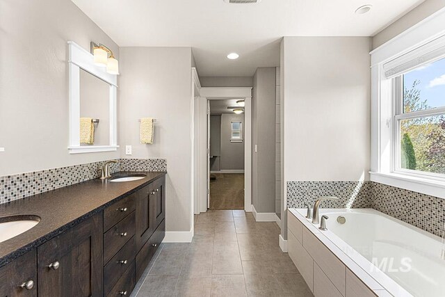 full bath featuring double vanity, a garden tub, baseboards, and a sink