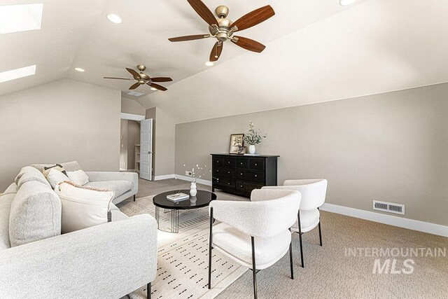 living area with baseboards, visible vents, ceiling fan, and vaulted ceiling with skylight