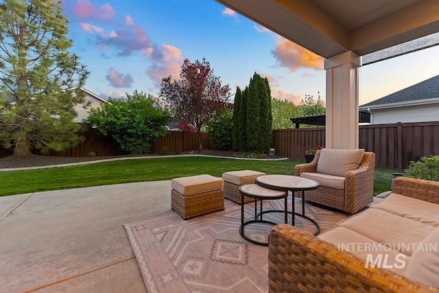 patio terrace at dusk featuring outdoor lounge area, a lawn, and a fenced backyard