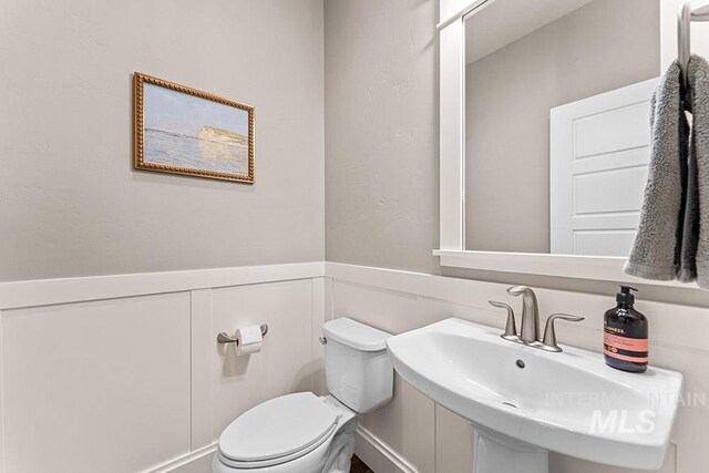 half bath with a wainscoted wall, a sink, a decorative wall, and toilet