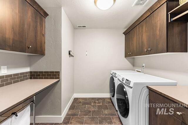 laundry room featuring a textured ceiling, washing machine and dryer, baseboards, visible vents, and cabinet space