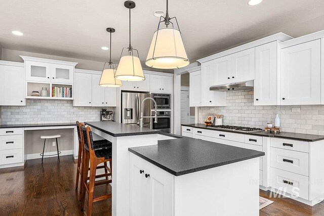 kitchen with backsplash, dark countertops, stainless steel appliances, and under cabinet range hood