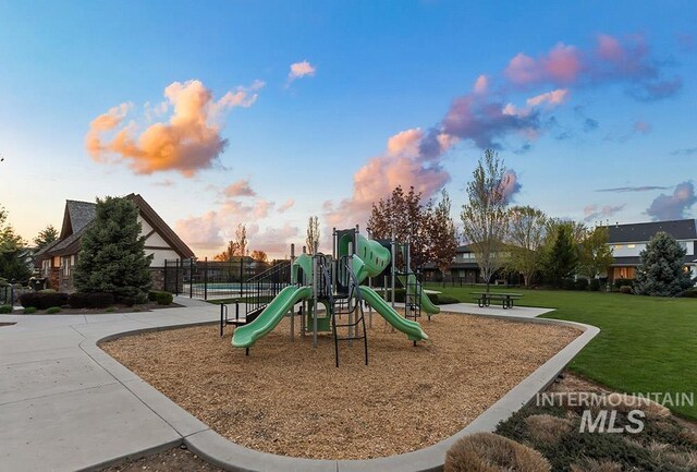 playground at dusk featuring a yard, fence, and playground community