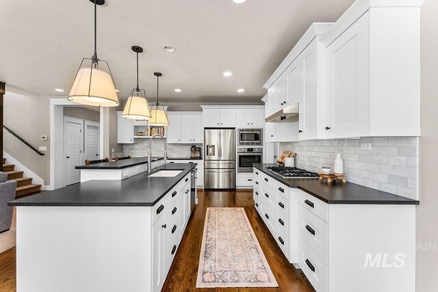 kitchen featuring dark wood-style flooring, dark countertops, a sink, appliances with stainless steel finishes, and under cabinet range hood