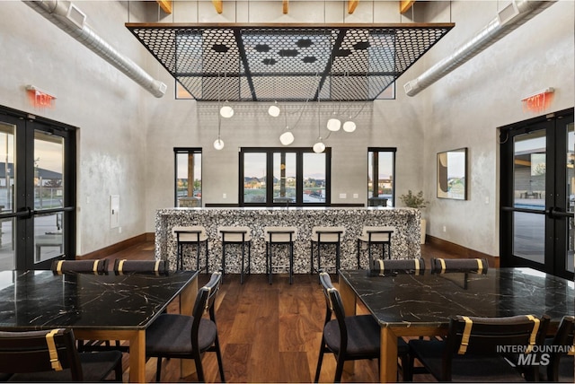 dining area featuring french doors, a towering ceiling, wood finished floors, and plenty of natural light
