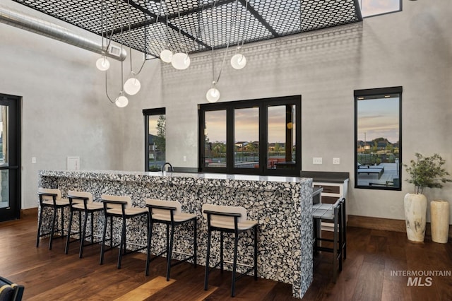 bar with a towering ceiling, dark wood finished floors, and baseboards