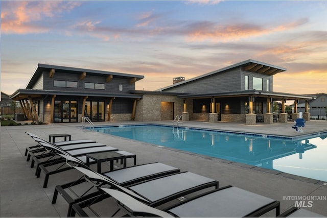 pool at dusk featuring a patio and a community pool