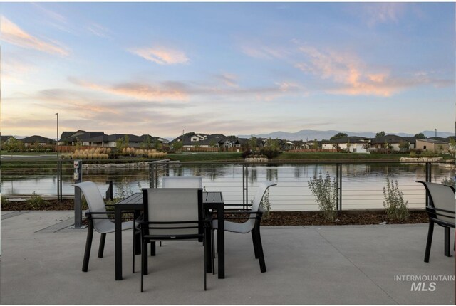 patio terrace at dusk featuring a water view, a residential view, and outdoor dining area
