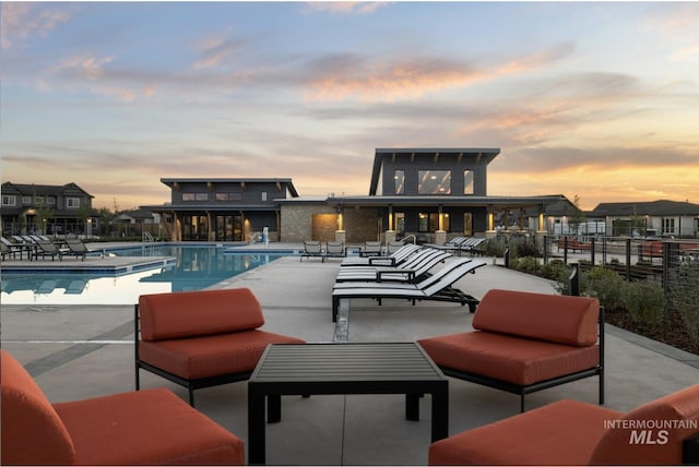 pool at dusk featuring a patio area, fence, and a community pool