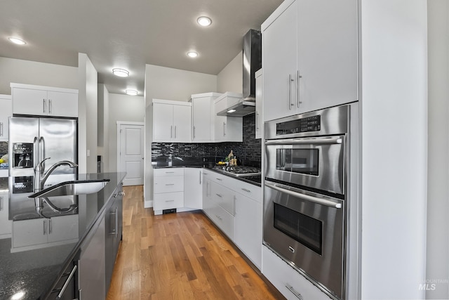 3924 E Forked Deer St, Boise, ID 83716 - kitchen featuring appliances with stainless steel finishes, wall chimney range hood, light wood-style floors, backsplash, and white cabinetry