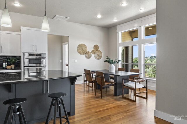 3924 E Forked Deer St, Boise, ID 83716 - kitchen featuring dark countertops, a kitchen breakfast bar, white cabinets, light wood-style floors, and decorative light fixtures