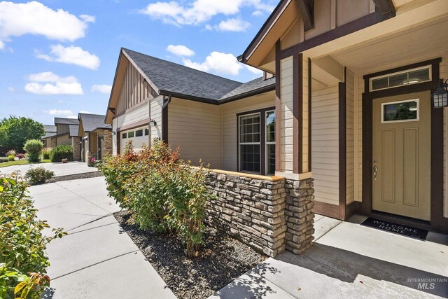 3924 E Forked Deer St, Boise, ID 83716 - view of exterior entry with board and batten siding, stone siding, roof with shingles, driveway, and an attached garage