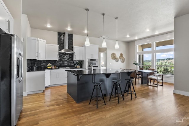 3924 E Forked Deer St, Boise, ID 83716 - kitchen featuring appliances with stainless steel finishes, wall chimney exhaust hood, dark countertops, a kitchen breakfast bar, and backsplash