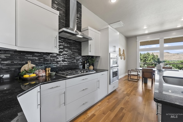 3924 E Forked Deer St, Boise, ID 83716 - kitchen with wall chimney exhaust hood, appliances with stainless steel finishes, tasteful backsplash, white cabinetry, and recessed lighting