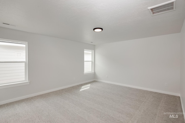 carpeted spare room with baseboards, visible vents, and a textured ceiling