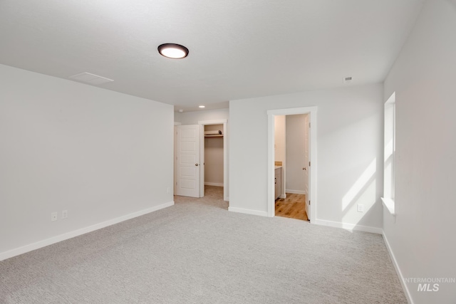 unfurnished bedroom featuring light carpet, ensuite bath, a closet, baseboards, and a spacious closet