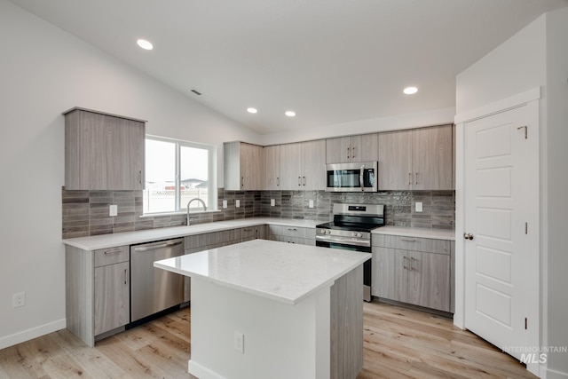 kitchen featuring a sink, lofted ceiling, light wood finished floors, and stainless steel appliances