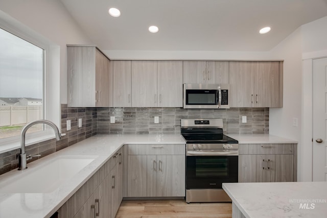 kitchen with light brown cabinetry, a sink, stainless steel appliances, decorative backsplash, and light stone countertops