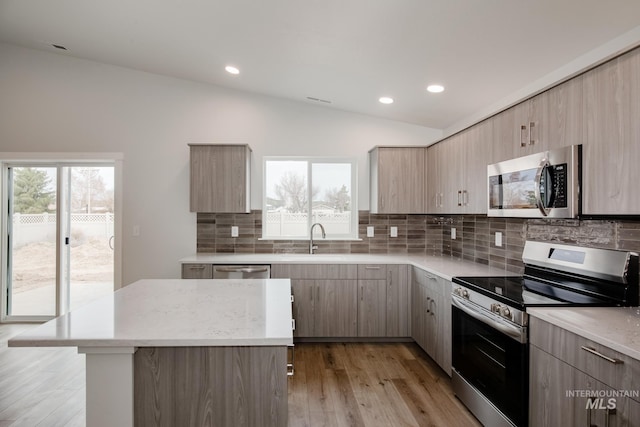 kitchen featuring vaulted ceiling, light wood-style floors, stainless steel appliances, modern cabinets, and a sink