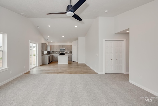 unfurnished living room featuring a ceiling fan, baseboards, high vaulted ceiling, recessed lighting, and light carpet