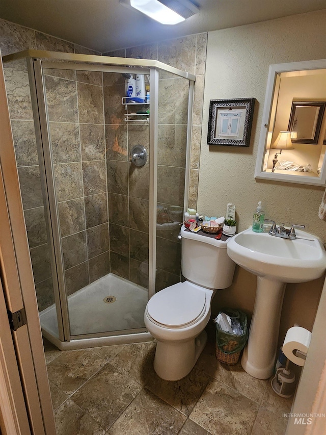 full bath with stone tile flooring, a textured wall, a shower stall, and toilet