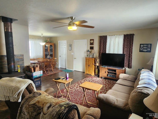 living area with ceiling fan, dark wood finished floors, and a wood stove