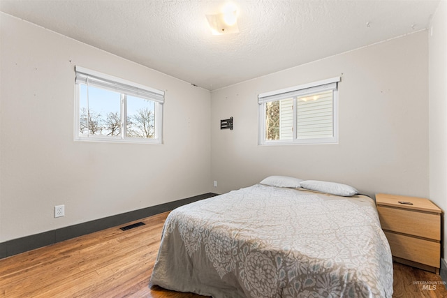 bedroom featuring a textured ceiling, hardwood / wood-style floors, and multiple windows