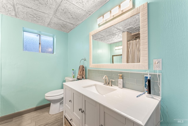 bathroom with tasteful backsplash, toilet, wood-type flooring, a paneled ceiling, and vanity