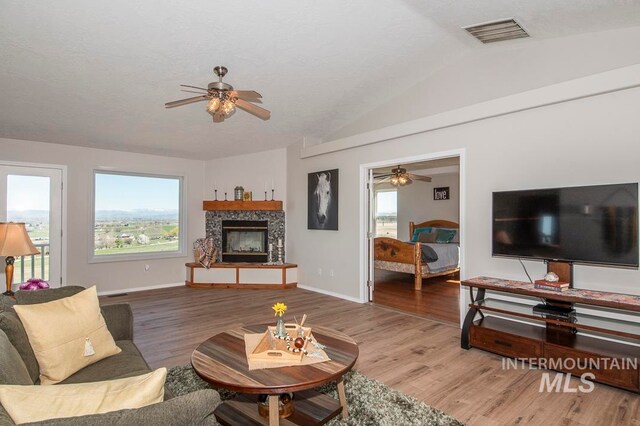 living room with vaulted ceiling, a fireplace, ceiling fan, and light wood-type flooring