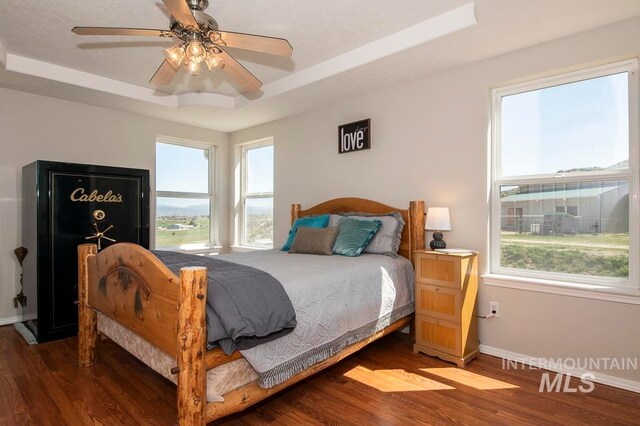 bedroom featuring ceiling fan, a raised ceiling, and dark wood-type flooring