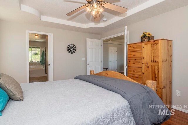 bedroom featuring a raised ceiling, ceiling fan, hardwood / wood-style flooring, and connected bathroom