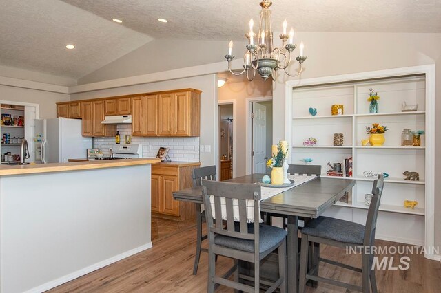 dining area with an inviting chandelier, lofted ceiling, a textured ceiling, and light hardwood / wood-style flooring