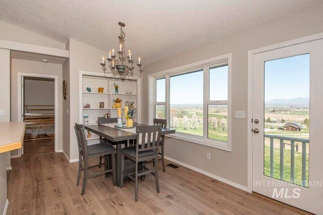 dining room featuring light hardwood / wood-style floors, a textured ceiling, vaulted ceiling, and a chandelier