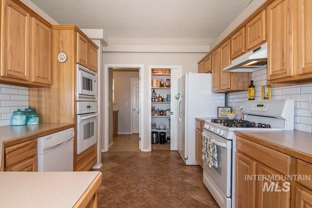 kitchen featuring backsplash, dark tile floors, and white appliances