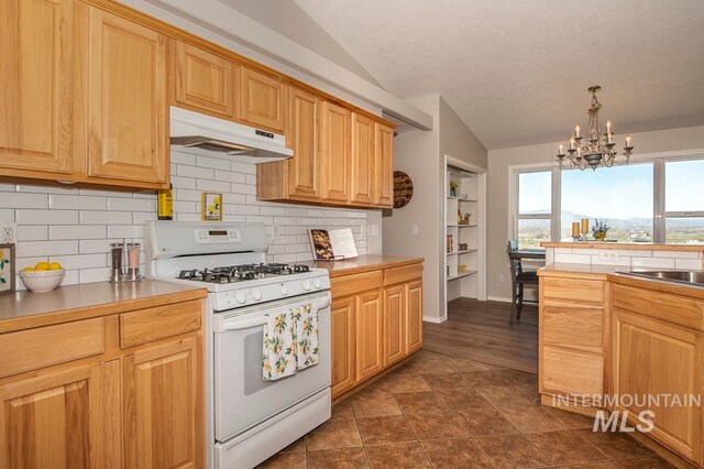 kitchen with a chandelier, white gas stove, dark tile flooring, lofted ceiling, and backsplash