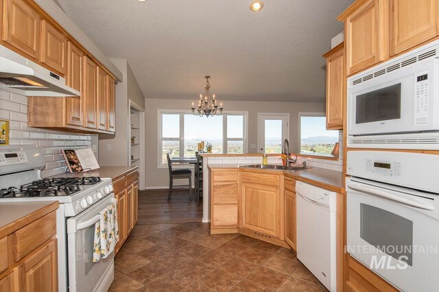 kitchen with white appliances, sink, dark tile flooring, backsplash, and an inviting chandelier