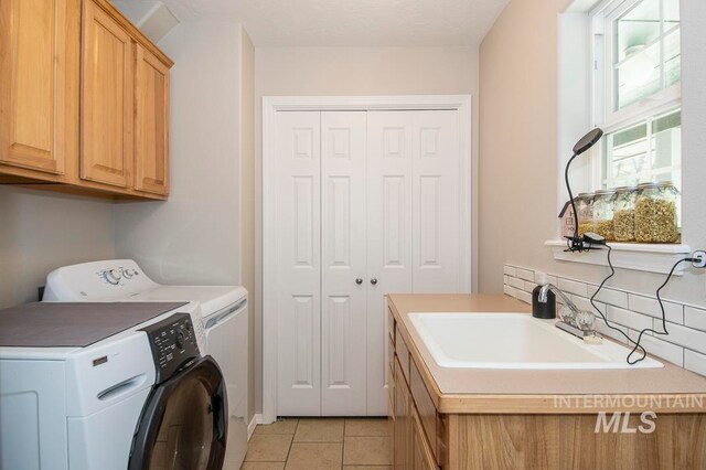 laundry area with washing machine and clothes dryer, light tile floors, cabinets, and sink