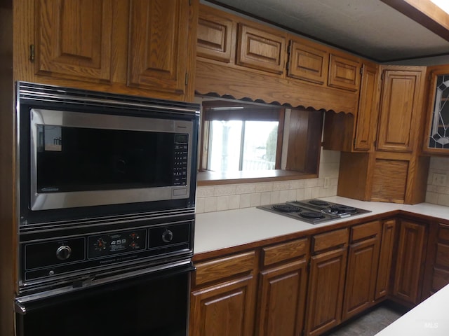 kitchen featuring stainless steel microwave, oven, cooktop, and backsplash