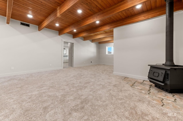 unfurnished living room with beamed ceiling, carpet flooring, a wood stove, and wooden ceiling