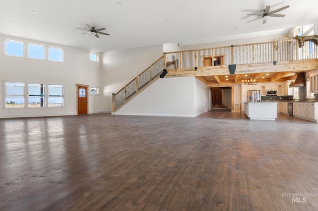 unfurnished living room featuring ceiling fan, a towering ceiling, and dark wood-type flooring