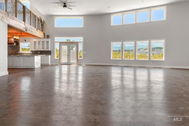 unfurnished living room featuring ceiling fan with notable chandelier, wood-type flooring, a towering ceiling, and french doors