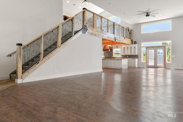 unfurnished living room with ceiling fan, dark hardwood / wood-style floors, a towering ceiling, and french doors