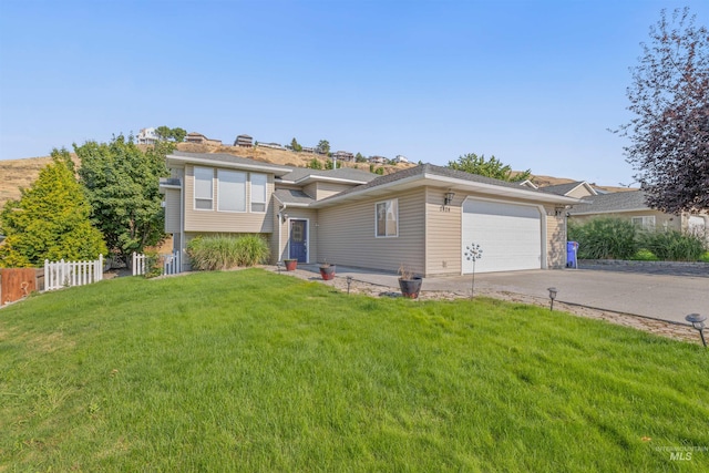 split level home featuring concrete driveway, an attached garage, fence, and a front yard